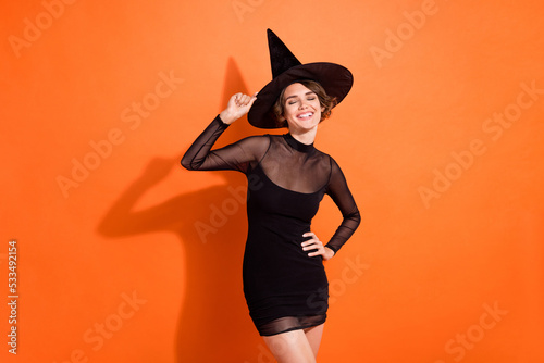 Photo of cute dreamy girl dressed black gothic dress arm headwear closed eyes smiling isolated orange color background