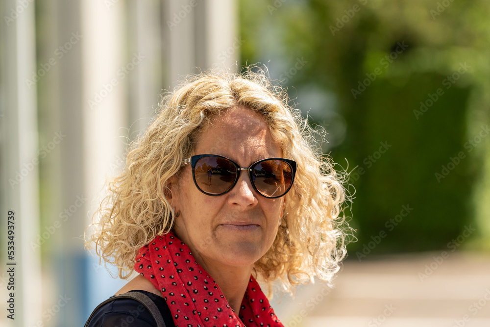 Woman smiling at the camera with blonde curls and sunglasses