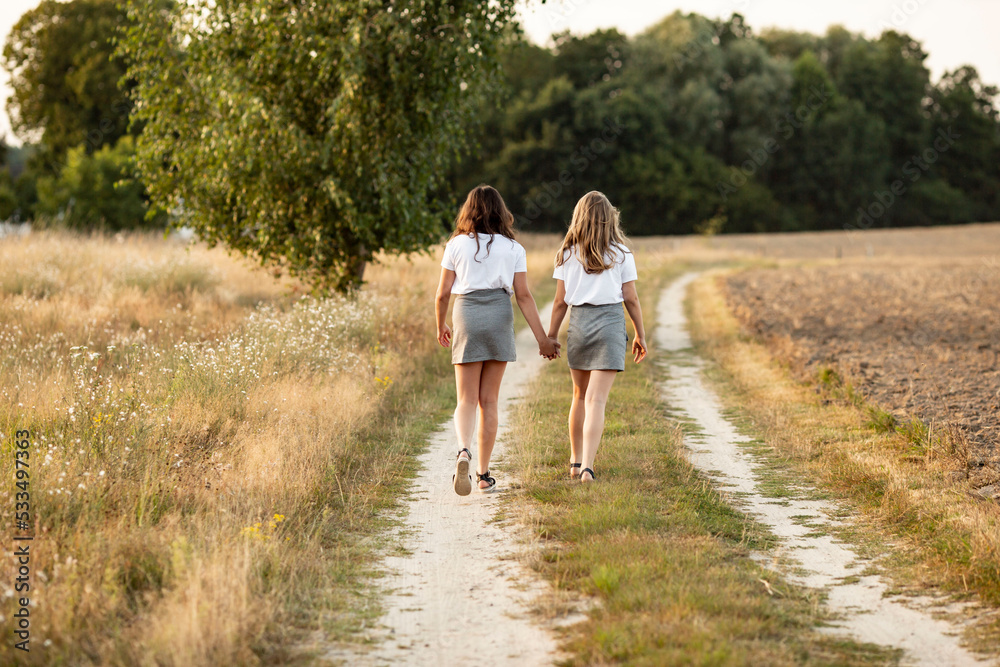 Two sisters holding their hands and walking on a path in the countryside at fall Two sisters holding their hands and walking on a path in the countryside at fall