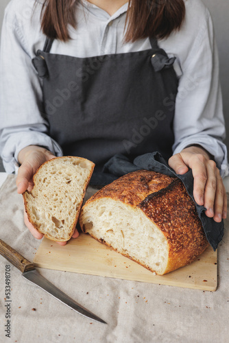 baker woman in a dark apron is cooking bread in the kitchen, a cook in a pastry shop is holding bread in her hands. fresh bread is on the cutting board. Baking and confectionery in a bakery or