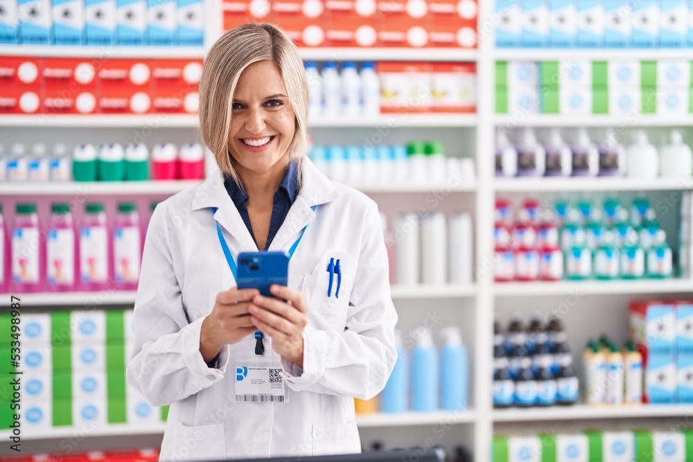 Young blonde woman pharmacist using smartphone working at pharmacy Young blonde woman pharmacist using smartphone working at pharmacy