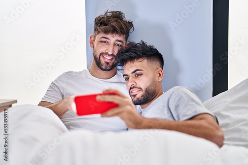 Young couple watching video on smartphone sitting on bed at bedrooom photo