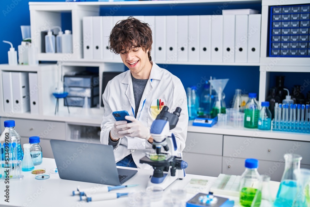 Young hispanic man scientist using smartphone and laptop at laboratory
