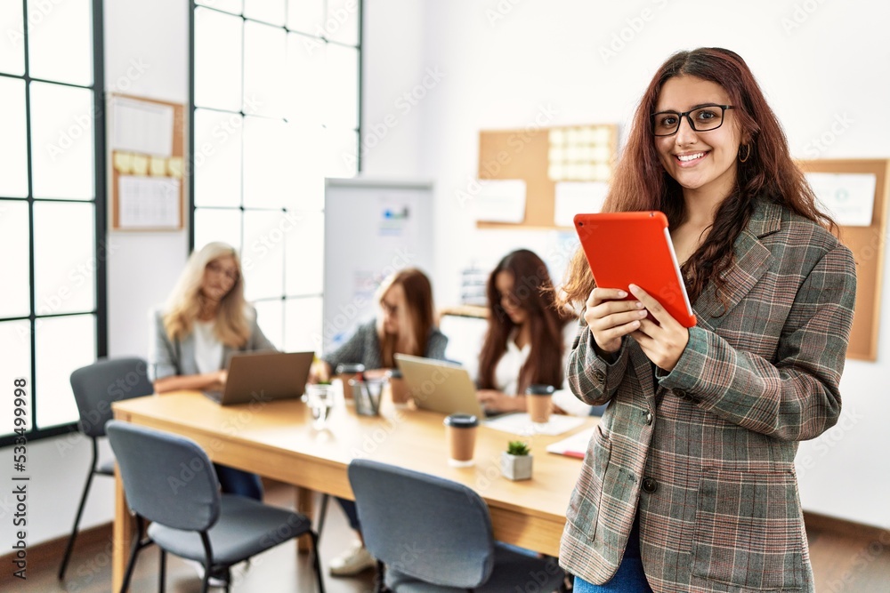 Young businesswoman smiling happy using touchpad while partners work at the office. Young businesswoman smiling happy using touchpad while partners work at the office.