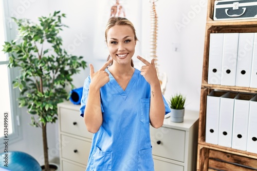 Young caucasian woman working at pain recovery clinic smiling cheerful showing and pointing with fingers teeth and mouth. dental health concept.