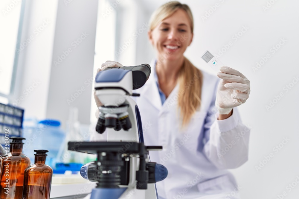 Young blonde woman wearing scientist uniform using microscope at laboratory Young blonde woman wearing scientist uniform using microscope at laboratory