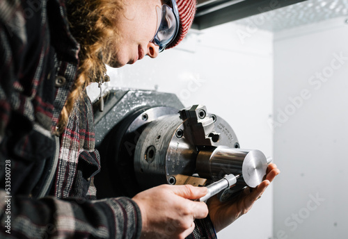 Konstfotografi Industrial woman machinist uses a CNC lathe machine and a micrometer for calibra