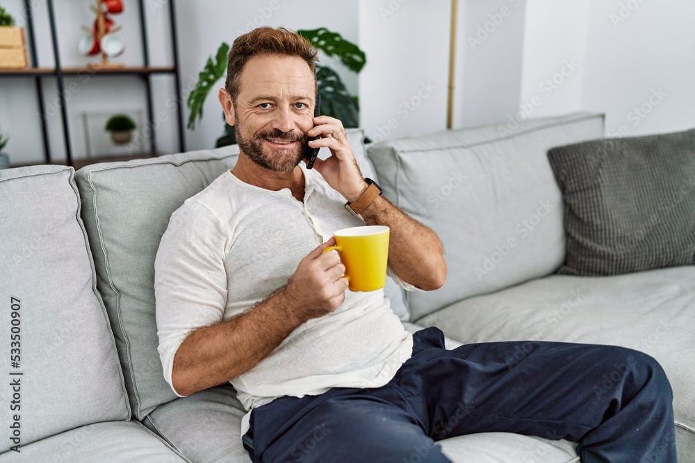 Middle age hispanic man talking on the smartphone drinking coffee at home Middle age hispanic man talking on the smartphone drinking coffee at home