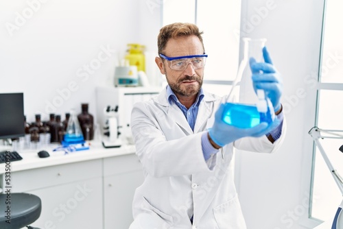 Middle age hispanic man wearing scientist uniform holding test tube at laboratory