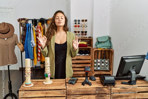 Beautiful hispanic woman working at fashion shop relax and smiling with eyes closed doing meditation gesture with fingers. yoga concept.