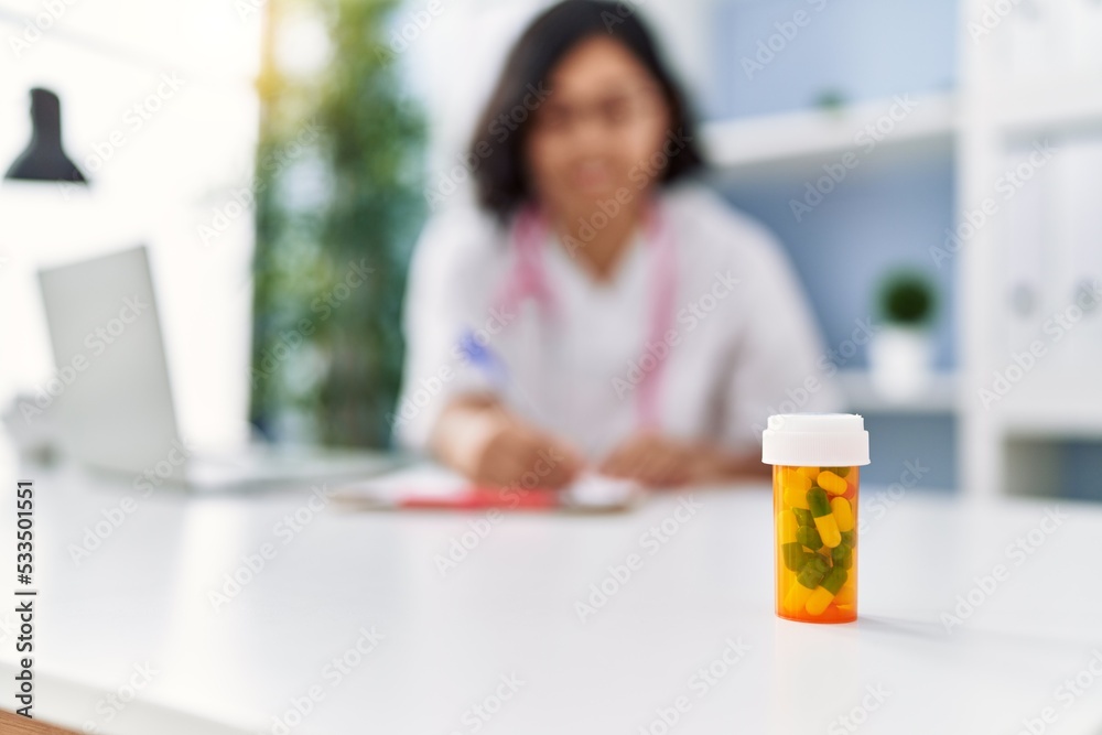 Young latin woman wearing doctor uniform prescribe pills at clinic