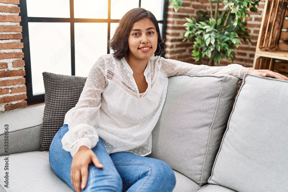 Obraz premium Young latin woman smiling confident sitting on sofa at home