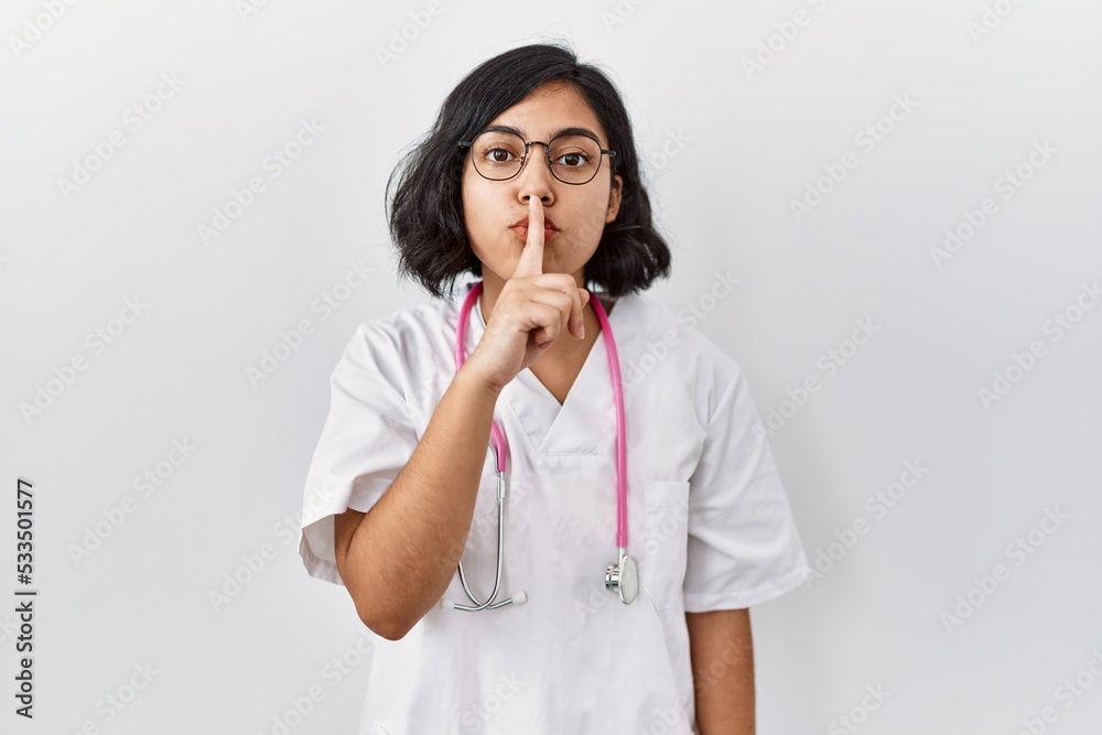Young hispanic doctor woman wearing stethoscope over isolated background asking to be quiet with finger on lips. silence and secret concept. Young hispanic doctor woman wearing stethoscope over isolated background asking to be quiet with finger on lips. silence and secret concept.