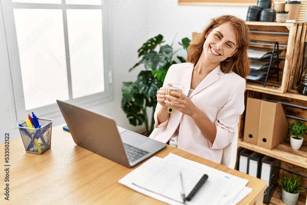 Young caucasian businesswoman smiling happy drinking tea working at the office. Young caucasian businesswoman smiling happy drinking tea working at the office.