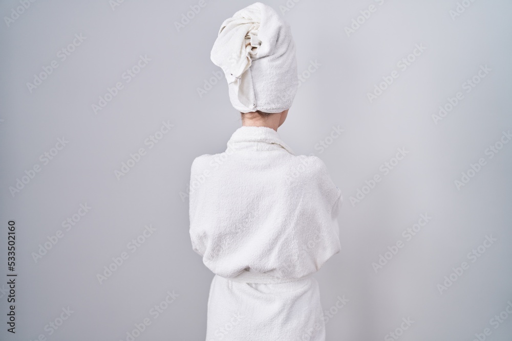 Blonde caucasian woman wearing bathrobe standing backwards looking away with crossed arms - obrazy, fototapety, plakaty 
