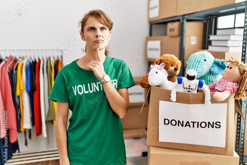 Beautiful caucasian woman wearing volunteer t shirt at donations stand thinking concentrated about doubt with finger on chin and looking up wondering