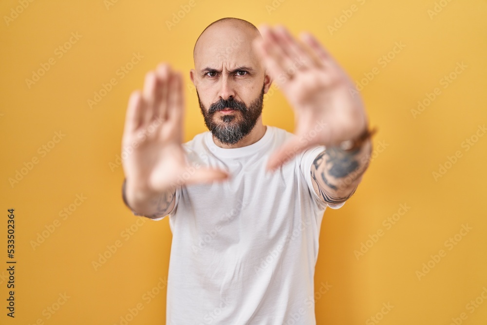 Young hispanic man with tattoos standing over yellow background doing frame using hands palms and fingers, camera perspective Young hispanic man with tattoos standing over yellow background doing frame using hands palms and fingers, camera perspective