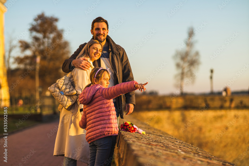 A happy family stands on a fortress overlooking the city and the river. They enjoy a beautiful day and a view.