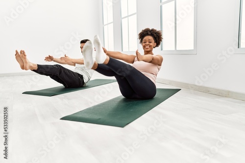 Young african american woman and hispanic man exercising at pilates room, stretching body and doing yoga pose, training strength and balance