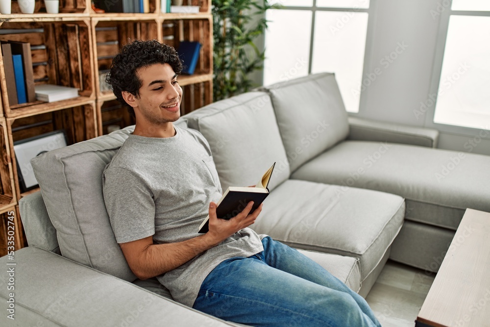 Young hispanic man reading book sitting on the sofa at home. Young hispanic man reading book sitting on the sofa at home.