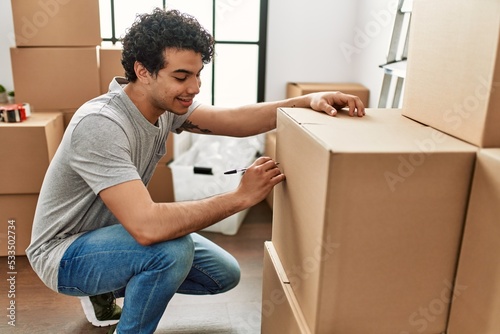 Young hispanic man smiling happy packing boxes at new home.
