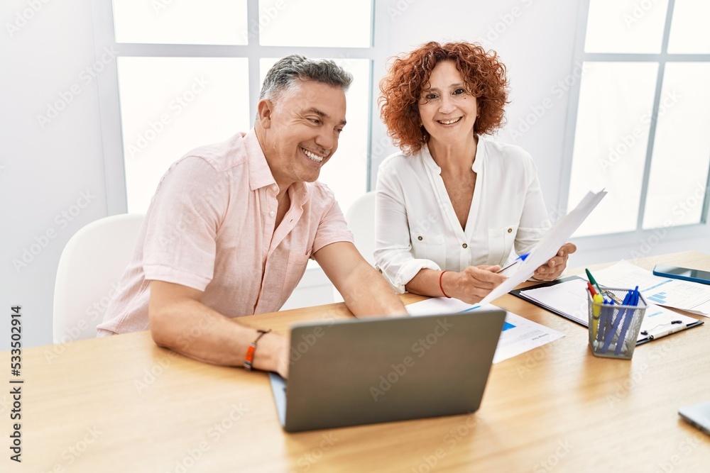 Middle age man and woman business workers using laptop and reading document at office Middle age man and woman business workers using laptop and reading document at office