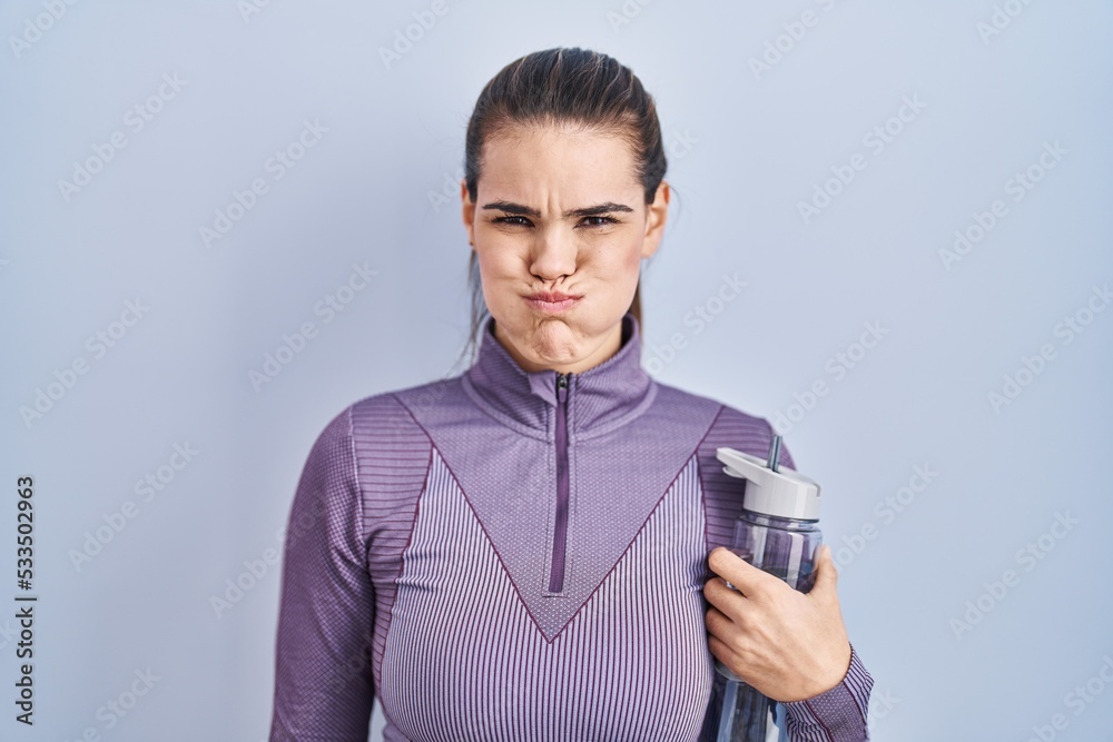 Beautiful woman wearing sportswear holding water bottle puffing cheeks with funny face. mouth inflated with air, crazy expression. Beautiful woman wearing sportswear holding water bottle puffing cheeks with funny face. mouth inflated with air, crazy expression.