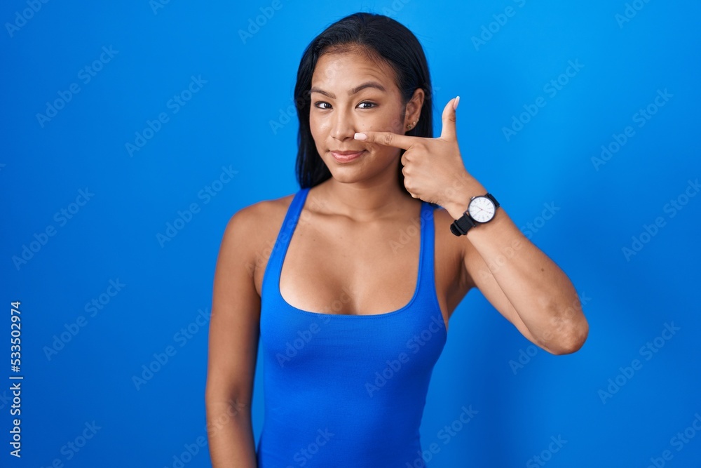 Hispanic woman standing over blue background pointing with hand finger to face and nose, smiling cheerful. beauty concept Hispanic woman standing over blue background pointing with hand finger to face and nose, smiling cheerful. beauty concept