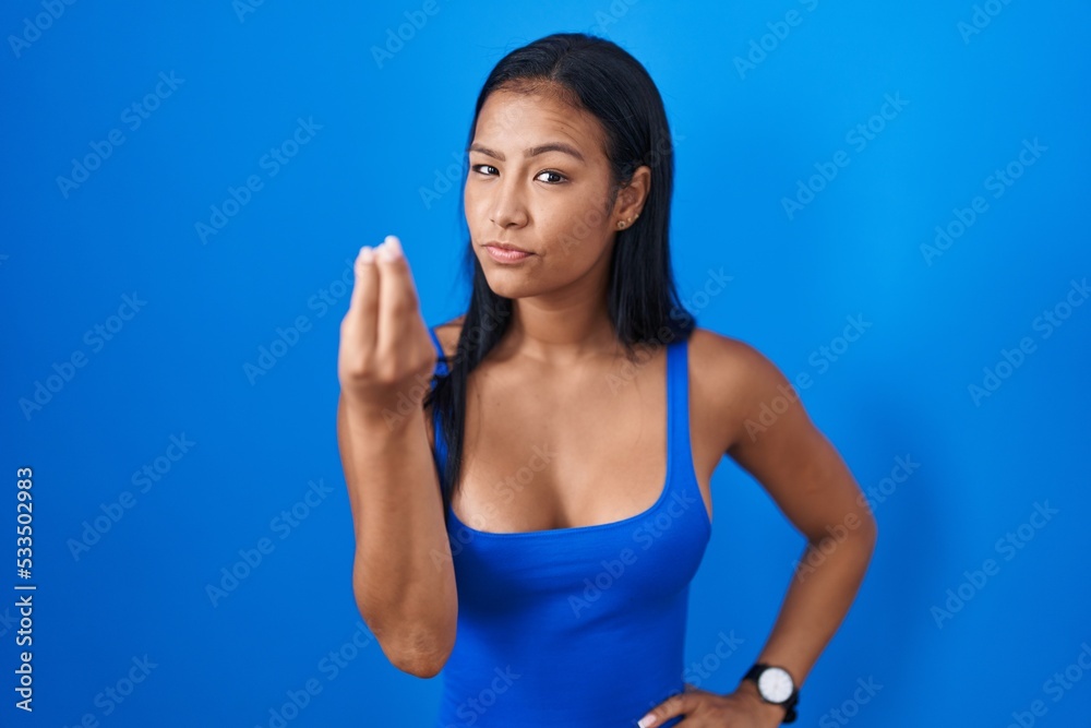 Hispanic woman standing over blue background doing italian gesture with hand and fingers confident expression Hispanic woman standing over blue background doing italian gesture with hand and fingers confident expression