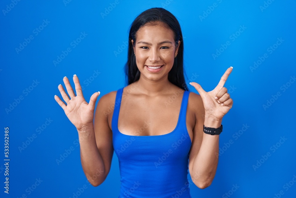Hispanic woman standing over blue background showing and pointing up with fingers number seven while smiling confident and happy. Hispanic woman standing over blue background showing and pointing up with fingers number seven while smiling confident and happy.