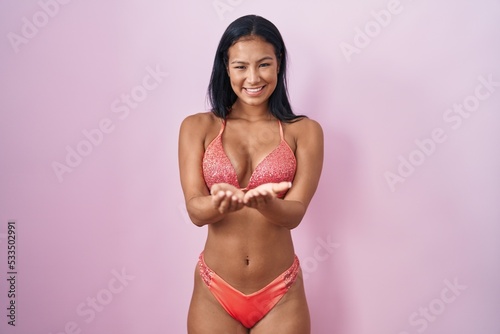 Hispanic woman wearing bikini smiling with hands palms together receiving or giving gesture. hold and protection