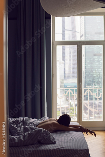 sexy brunette woman lies with her back on the bed in front of the bedroom window. © saulich84