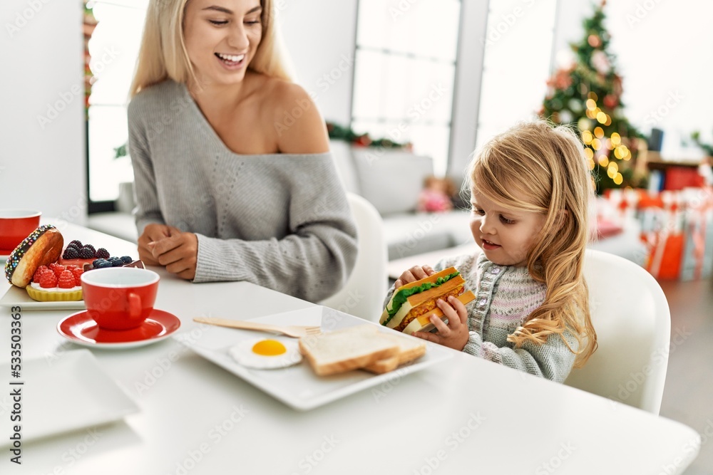 Mother and daughter having breakfast sitting by christmas tree at home Mother and daughter having breakfast sitting by christmas tree at home