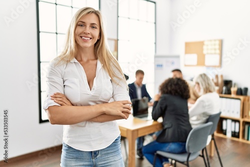Young caucasian businesswoman smiling happy standing with arms crossed gesture at the office during business meeting.