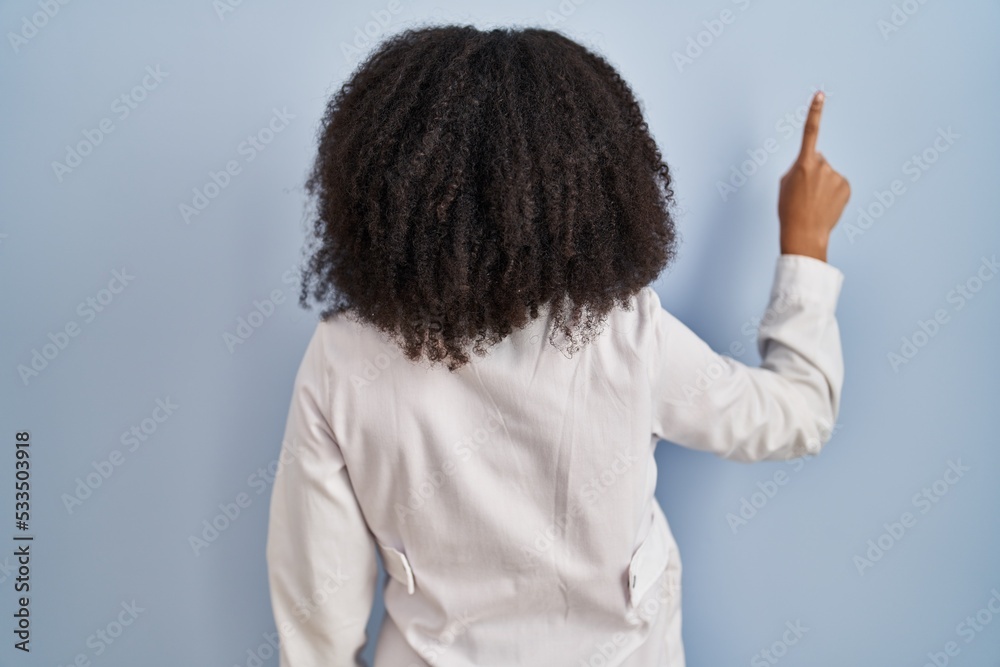 Young african american woman wearing doctor uniform and stethoscope posing backwards pointing ahead with finger hand Young african american woman wearing doctor uniform and stethoscope posing backwards pointing ahead with finger hand