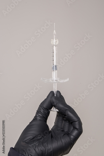 hands with disposable black gloves holding syringe