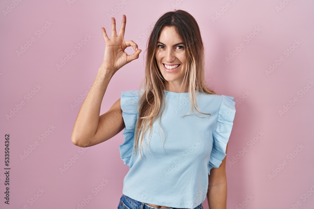 Young hispanic woman standing over pink background smiling positive doing ok sign with hand and fingers. successful expression. Young hispanic woman standing over pink background smiling positive doing ok sign with hand and fingers. successful expression.