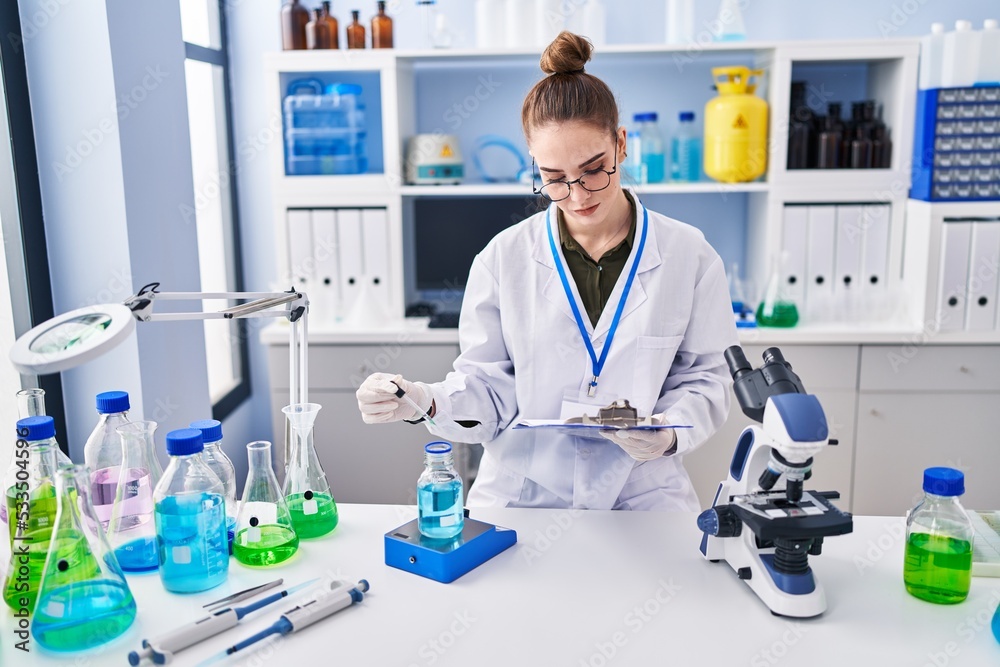 Young woman scientist reading document measuring liquid at laboratory Young woman scientist reading document measuring liquid at laboratory