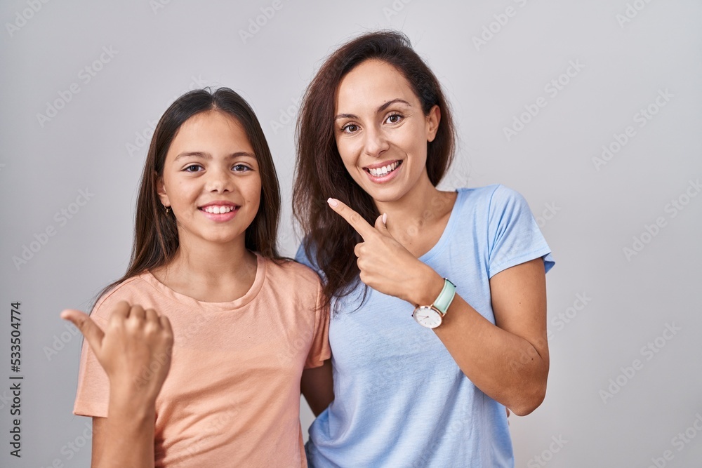 Young mother and daughter standing over white background cheerful with a smile on face pointing with hand and finger up to the side with happy and natural expression Young mother and daughter standing over white background cheerful with a smile on face pointing with hand and finger up to the side with happy and natural expression