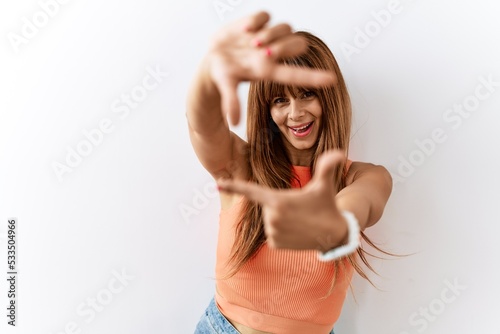 Hispanic woman with bang hairstyle standing over isolated background smiling making frame with hands and fingers with happy face. creativity and photography concept.