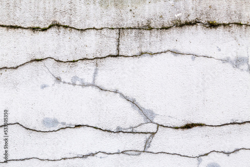 Textured grey white, concrete wall with heavy black cracks and grungy, rough painted, detail. Design element abstract background with holes, paint patches, scratches and weathering.