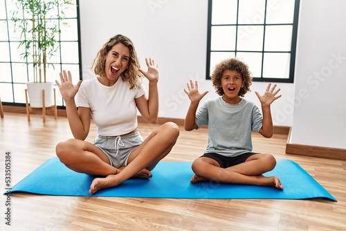 Young woman and son sitting on training mat at the gym celebrating victory with happy smile and winner expression with raised hands