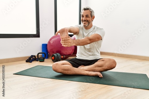 Middle age grey-haired man smiling confident stretching arm at sport center