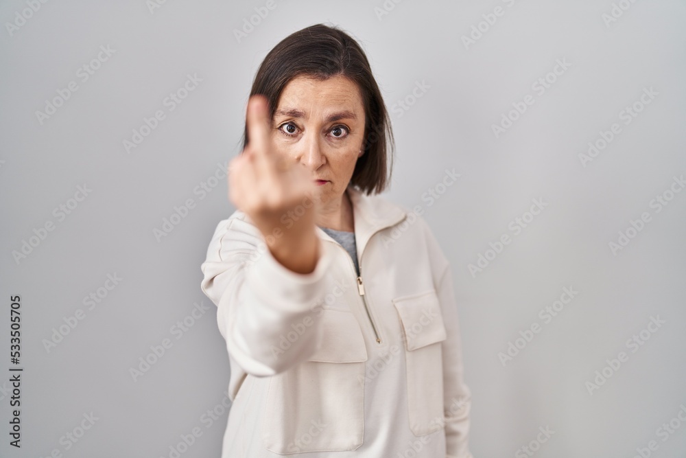Middle age hispanic woman standing over isolated background showing middle finger, impolite and rude fuck off expression Middle age hispanic woman standing over isolated background showing middle finger, impolite and rude fuck off expression