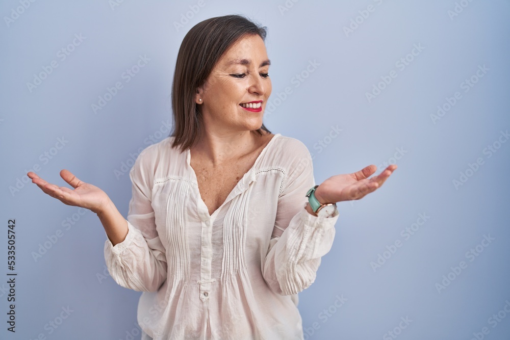 Middle age hispanic woman standing over blue background smiling showing both hands open palms, presenting and advertising comparison and balance Middle age hispanic woman standing over blue background smiling showing both hands open palms, presenting and advertising comparison and balance