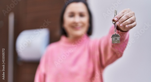 Middle age woman smiling confident holding key of new home at street