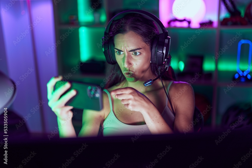 Young brunette woman playing video games with smartphone pointing with finger to the camera and to you, confident gesture looking serious Young brunette woman playing video games with smartphone pointing with finger to the camera and to you, confident gesture looking serious