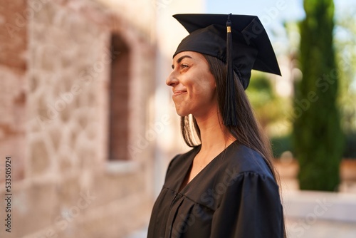 Young hispanic woman wearing graduated uniform standing at university photo