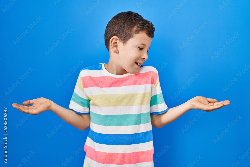 Young caucasian kid standing over blue background smiling showing both hands open palms, presenting and advertising comparison and balance Young caucasian kid standing over blue background smiling showing both hands open palms, presenting and advertising comparison and balance