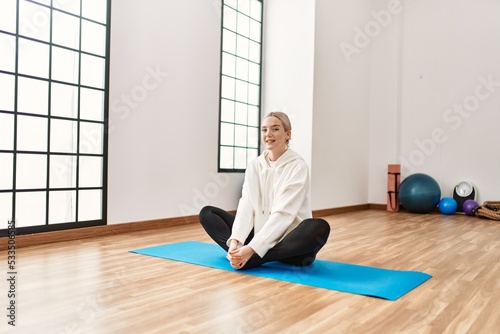 Young blonde girl smiling happy stretching at sport center.